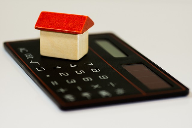 a small toy house made of wood with a red roof sits on top of a black calculator on a white background